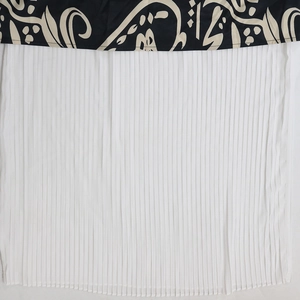 Detail eines Kaftankleids mit schwarzem Ethno-Druck und weißem Plissee-Chiffon-Saum