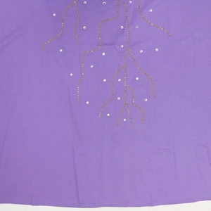 Détail de robe ample violette avec motifs de perles dorées et strass scintillants