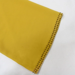 Macro detail of yellow mesh dress sleeve featuring intricate amber rhinestone embellishments