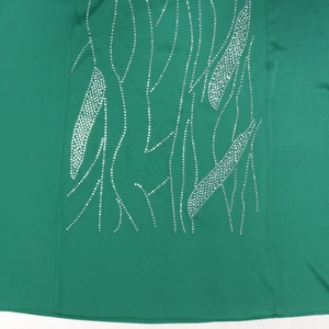 Macro detail of green satin dress fabric featuring intricate silver rhinestone patterns