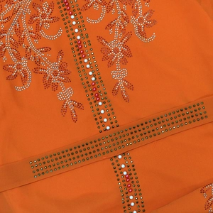 Detailed macro view of orange mesh dress with intricate beadwork and floral rhinestones