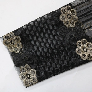 Detail von schwarzem Netzgewebe mit goldener Blumenstickerei und 3D-Blütenapplikationen