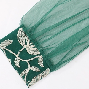 Detail view of intricate leaf embroidery on dark green mesh sleeve fabric