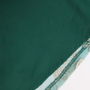 Close-up of intricate feather embroidery on sheer mesh hem of a dark green kaftan dress