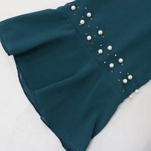 Detail of dark teal chiffon dress with pearl beading and ruffled hemline finish