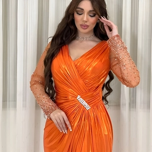 Detail of the high-slit orange evening gown featuring a diamond buckle and beaded sleeves