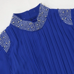 Détail d'une robe plissée bleu roi avec des strass argentés et des perles sur l'encolure