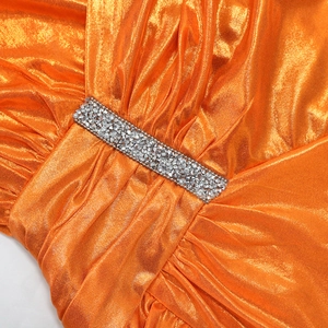 Detail of metallic orange gown featuring pleated fabric and sparkling rhinestone trim