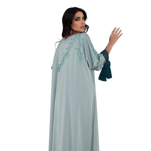 Détail de broderie de perles bleues et dorées sur caftan en satin bleu clair avec des nœuds