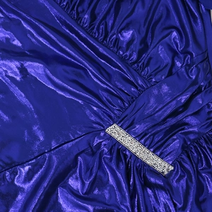 Close-up of royal blue metallic evening gown with pleated waist and silver rhinestone trim