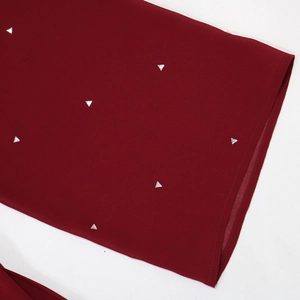Détail du tissu en mousseline rouge vin avec des strass argentés en forme de triangle