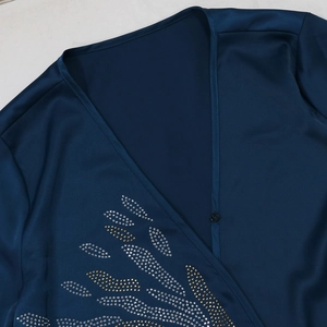 Dettaglio dello scollo a V in raso blu navy con ricamo a foglia di strass e bottone a pressione