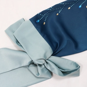 Détail de la robe en satin avec strass bleus et nœud décoratif vert menthe