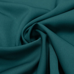 Close-up of dark teal twill fabric with elegant spiral folds showing drape and texture