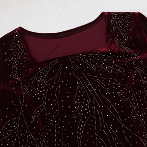 Macro detail of wine red velvet fabric with square neckline and intricate rhinestone pattern
