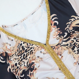 Dettaglio scollo a V di un abito caftano con strass dorati e stampe leopardate barocche