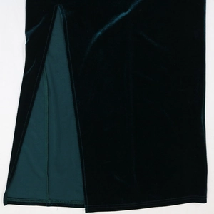 Detailed close-up of dark green velvet dress featuring a high side slit and fine stitching