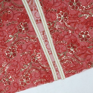 Détail du tissu en maille rouge avec broderie florale en paillettes dorées et ruban tissé