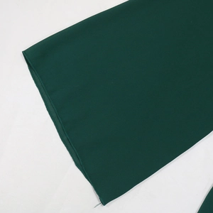 Detailed close-up of dark green chiffon fabric showing high-quality overlock stitching edge