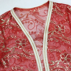 Détail macro du tissu en maille rouge avec broderies pailletées dorées et galon tissé
