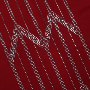 Macro detail of silver rhinestones in geometric patterns on deep red chiffon fabric