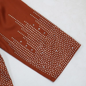 Détail de la manche en satin caramel ornée de motifs complexes en strass argentés