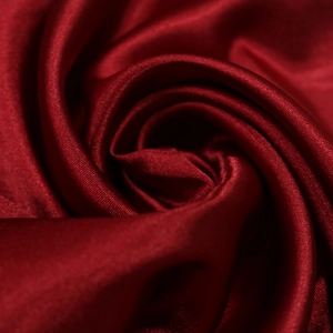 Dettaglio macro del tessuto satinato rosso vino con texture lucida e drappeggio setoso