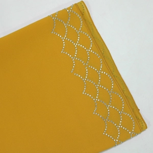 Close-up of mustard yellow fabric featuring geometric rhinestone pattern and fine stitching