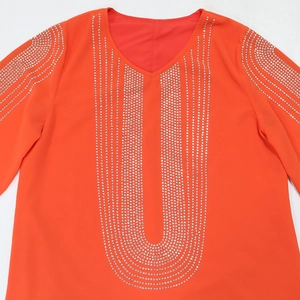 Dettaglio della tunica arancione con scollo a V e motivi geometrici in strass argento