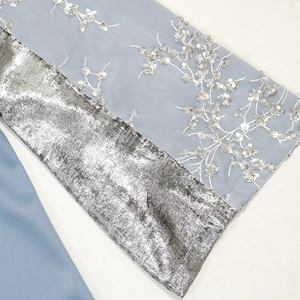 Detail eines hellblauen Netzkleides mit silbernen Paillettenblumen und Metallic-Manschette