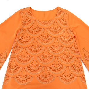 Détail d'un haut orange à col rond avec des motifs en strass et des manches longues élégantes