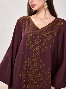 Détail du col en V avec paillettes dorées et strass sur la robe couleur bordeaux