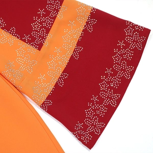 Détail de tissu rouge et orange orné de strass argentés en forme d'étoiles brillantes