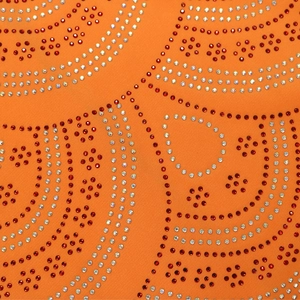 Détail du tissu orange avec des motifs floraux complexes en strass rouges et argentés