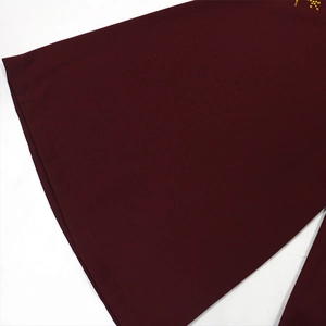 Détail de la robe bordeaux à col en V montrant les coutures fines et les strass dorés