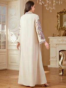 Détail de la broderie colorée et des sequins sur le col en V et les manches d'une robe ivoire