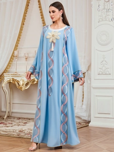 Détail de broderies florales et de pompons sur une robe caftan ethnique bleu clair
