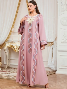 Détail de broderie florale et pompons blancs sur une robe longue ethnique rose à manches