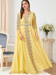 Detail of golden embroidery on long yellow kaftan dress with V-neck and matching belt
