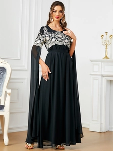 Détail d'une robe noire en mousseline avec broderies dorées et manches style cape