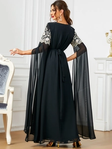 Détail d'une robe longue en maille noire avec broderie florale et manches fendues cape