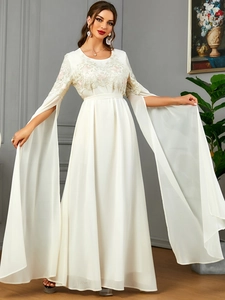 Détail d'une robe longue blanche à broderies florales et manches cape fendues