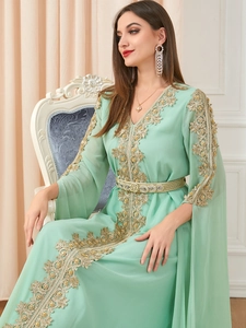 Detailed embroidery on a mint green Moroccan kaftan with gold patterns and belt