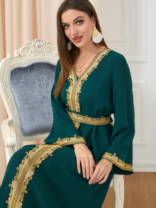 Detailed close-up of golden baroque embroidery on a dark green V-neck kaftan dress