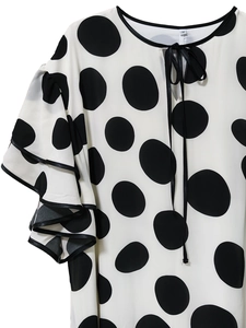 Close-up of polka dot dress featuring tiered ruffle sleeves and a neckline tie detail