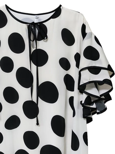 Detail of white polka dot top featuring ruffled sleeves and black ribbon neck tie