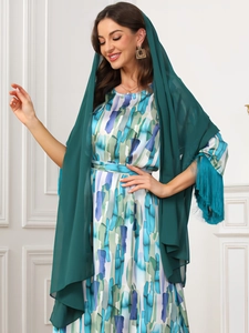 Detail of abstract print maxi dress with long fringed shawl and gold earrings on a model