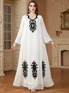 Détail de la broderie noire et dorée élégante sur une robe caftan blanche à manches longues