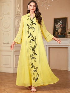 Detail of elegant yellow maxi dress featuring black embroidery and lace trumpet sleeves