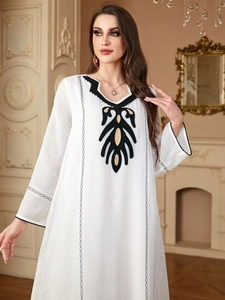 Détail de robe en coton blanc avec broderie feuille noire et dorée et dentelle ajourée